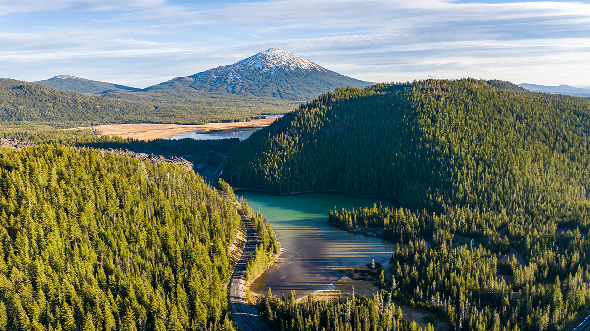 Aerial view of the Cascade Lakes Scenic Byway winding past a turquoise lake with Mount Bachelor in the background near Bend, Oregon