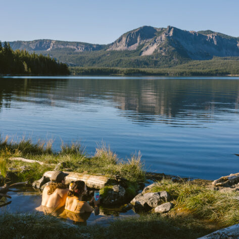 A man and woman soaking in Paulina Hot Springs and looking at the lake and mountain beyond