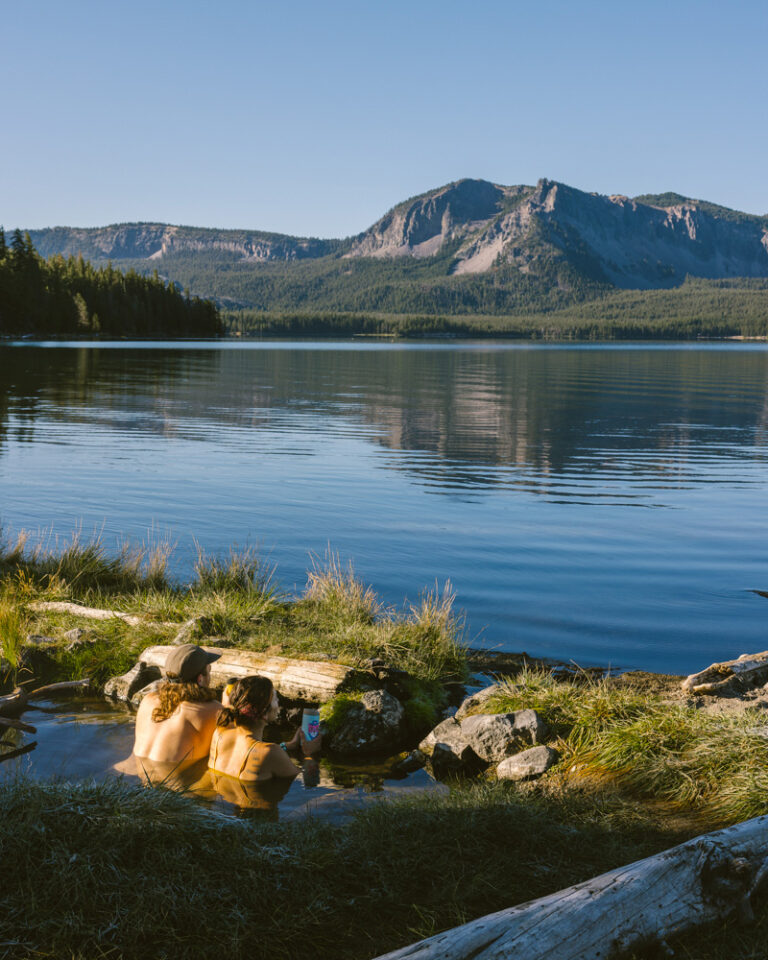 A man and woman soaking in Paulina Hot Springs and looking at the lake and mountain beyond