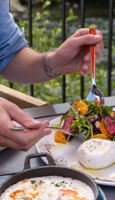 Close-up of a diner enjoying a colorful salad with burrata and citrus at Riverhouse on the Deschutes, seated at a riverside table overlooking the Deschutes River.