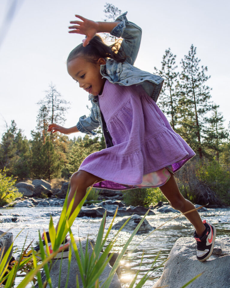 A little girl in a purple dress crossing a creek in Bend, OR