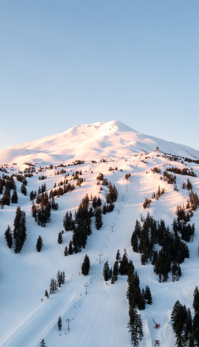 A sunrise view of Mt. Bachelor’s snow-covered slopes in Bend, Oregon, showing groomed runs, chairlifts, and alpine terrain—an iconic scene featured in this Mt. Bachelor ski guide highlighting the mountain’s best runs, insider tips, and ways to score the best ski deals at one of the most affordable major ski resorts in the West.