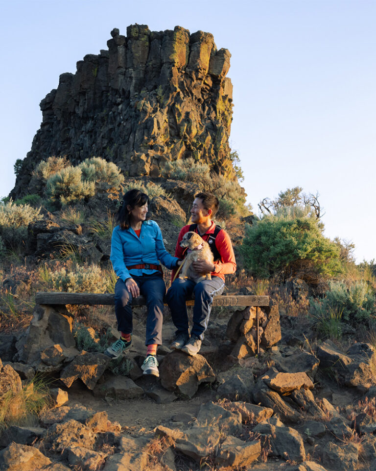 Couple with their dog enjoying golden-hour views on a high-desert hike near Bend, Oregon during spring — a classic spring in Bend Oregon itinerary blending best spring skiing and hiking with scenic canyon trails.
