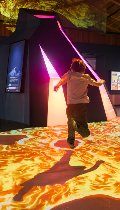 A child jumps over a glowing lava floor projection inside the Under Pressure volcanic exhibit at the High Desert Museum in Bend, Oregon