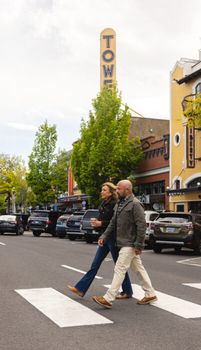 A couple crosses a downtown Bend street in front of the Tower Theatre on a sunny summer day.