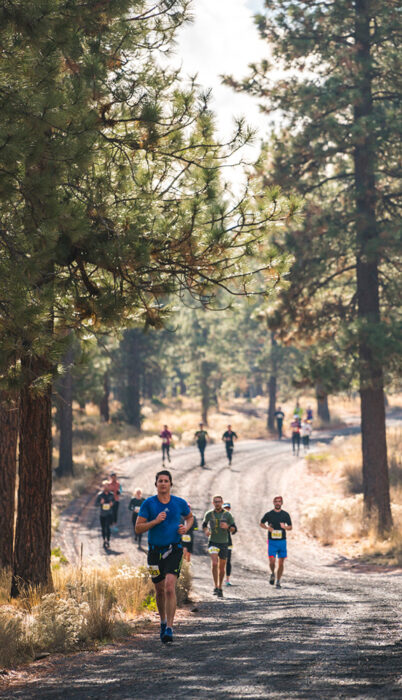 Trail runners racing through a pine forest on a gravel road during a summer trail race near Bend, Oregon